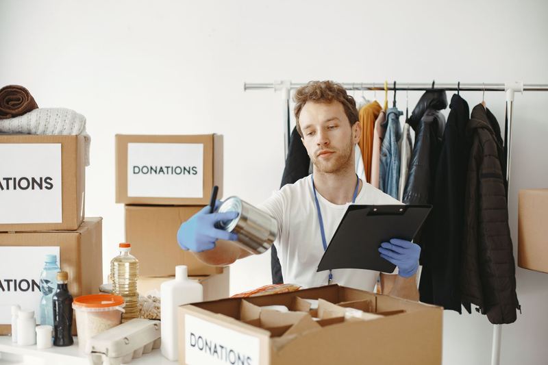 A nonprofit staffer with a clipboard among donation boxes and a clothing rack