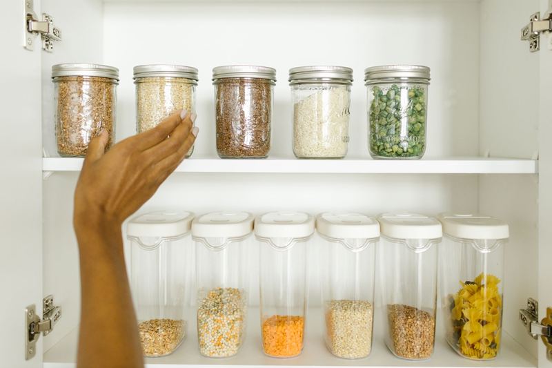 A hand restocking jars on a pantry shelf
